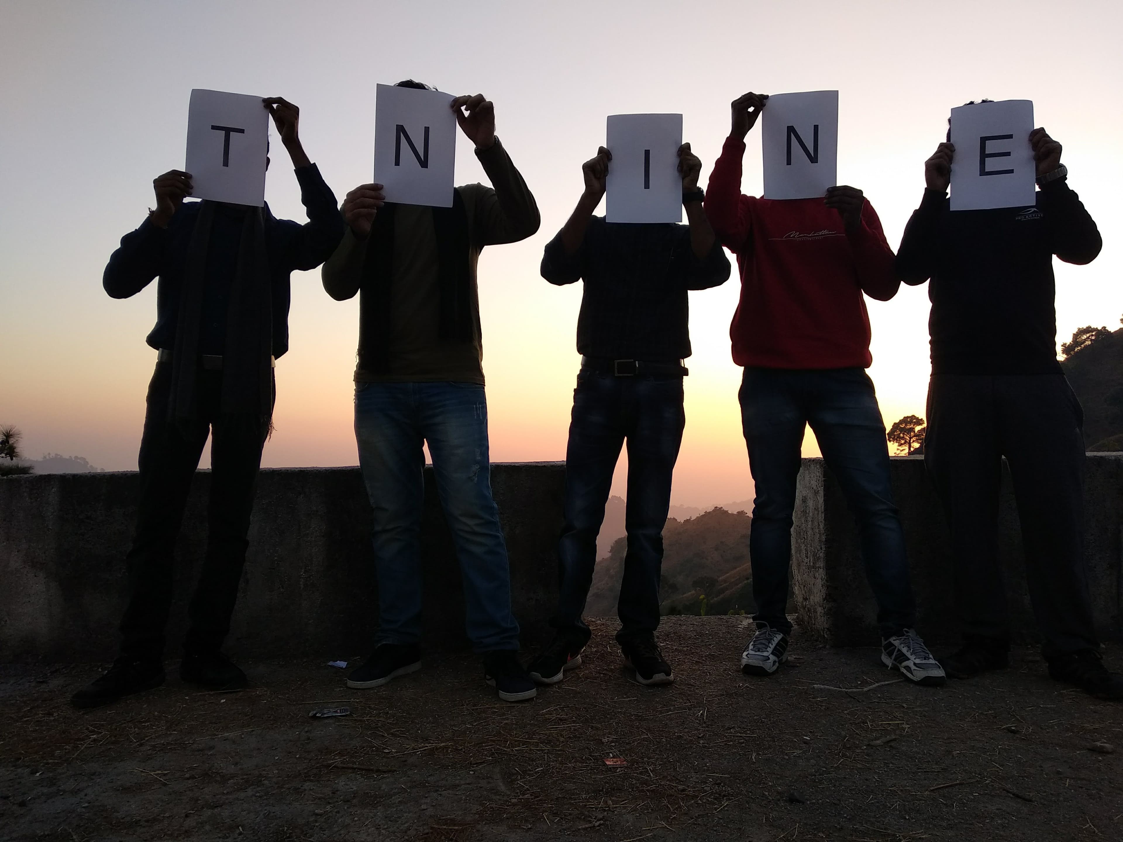 Five TNine Innovations co-founders holding up letter cards spelling T-N-I-N-E at sunset
